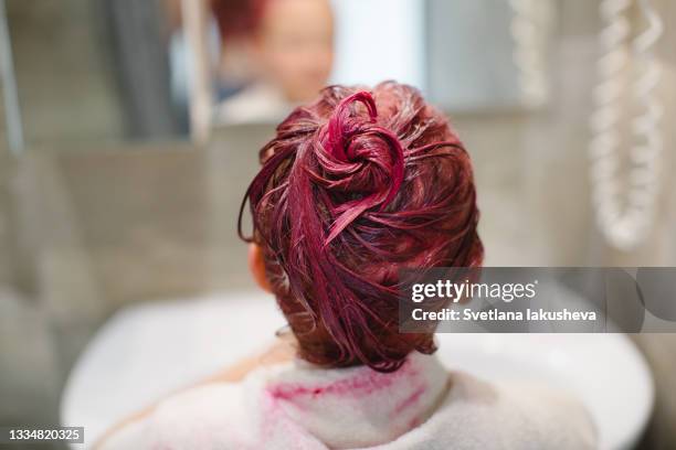 an elementary school age girl dyes her hair pink with a white towel over her shoulders in a gray bathroom near the sink and mirror. back view, focus on hair. - kid girl towel stock pictures, royalty-free photos & images