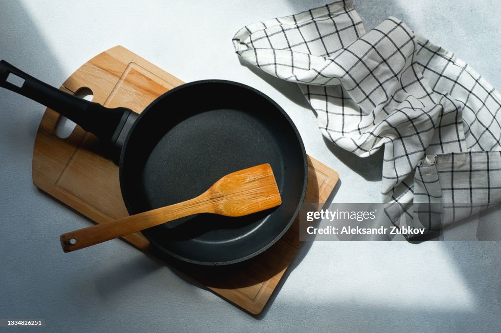 A New Clean Empty Cast-Iron Frying Pan And A Wooden spatula, on a cutting board. The concept of cooking in a restaurant and cafe, at home in the kitchen. Cook yourself, taking courses on the ability to cook delicious and beautiful food.