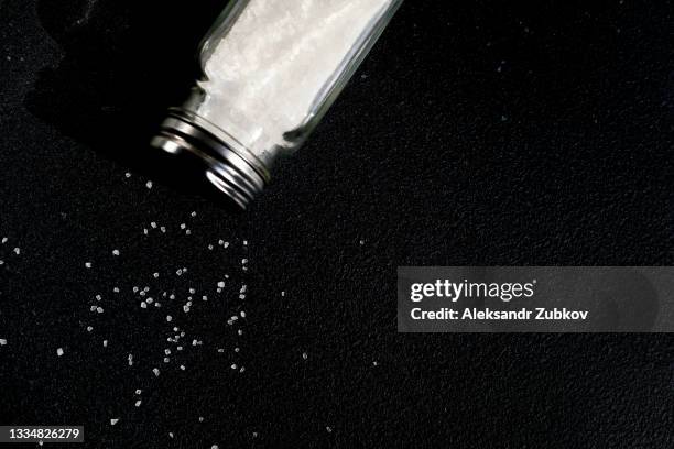 natural, organic, sea, white salt, poured from a fallen salt shaker, on a black table or background. the concept of cooking healthy food, cosmetology. copy of the text space. - salt shaker stockfoto's en -beelden