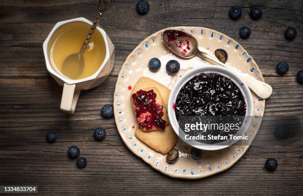 blueberry jam in a bowl and fresh blueberries served with tea and biscuits on a wooden table - blueberries in bowl stock pictures, royalty-free photos & images