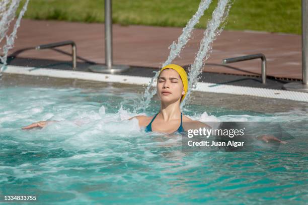 front view of a latina female in hydrotherapy waterfall jet in swimming pool - algar waterfall spain stock pictures, royalty-free photos & images