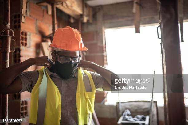 construction worker dressing his uniform and protective workwear at a construction site - face mask protective workwear stockfoto's en -beelden