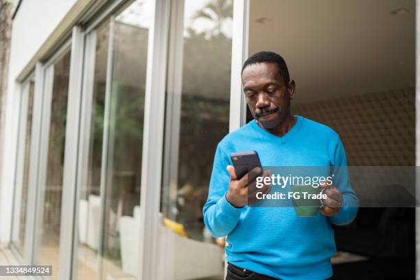 senior man looking at smartphone at home - african on phone stockfoto's en -beelden