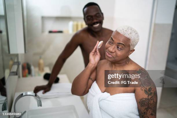 mature woman applying cleansing lotion to face with husband in the bathroom at home - woman applying cotton ball stock pictures, royalty-free photos & images