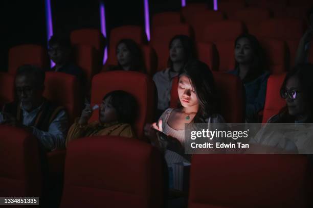 asian chinese woman reading phone message during cinema movie show time in the dark ignoring ansd disturbing other audience around her - inconvenience stock pictures, royalty-free photos & images