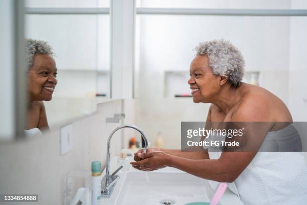 ältere frau, die sich zu hause im badezimmer die hände wäscht - senioren in bad stock-fotos und bilder