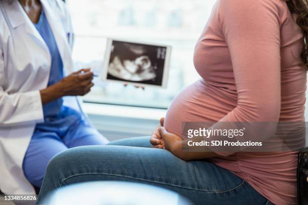 fokus auf den vordergrund, wenn arzt ultraschall im hintergrund zeigt - pregnant woman at doctor stock-fotos und bilder