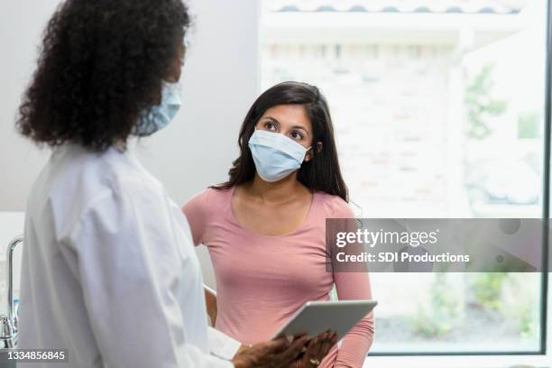 mujer con mascarilla protectora escucha las noticias del médico - masks fotografías e imágenes de stock