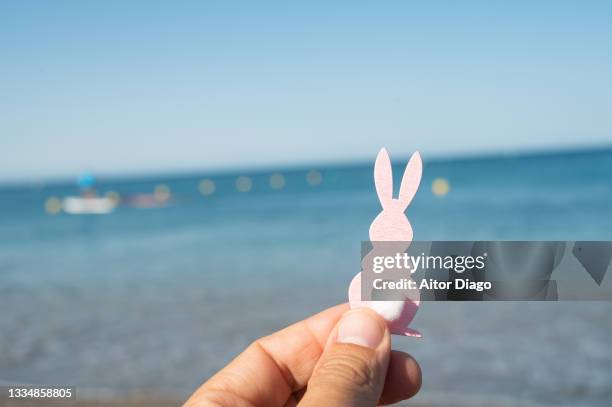 a person holds an easter bunny figurine in his hand on a beach at the shore of the beach. - easter bunny man stock pictures, royalty-free photos & images