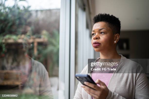 woman contemplating using smartphone at home - stress emotivo imagens e fotografias de stock