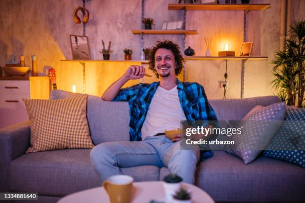 man watching movie and eating potato chips - man sofa stock pictures, royalty-free photos & images