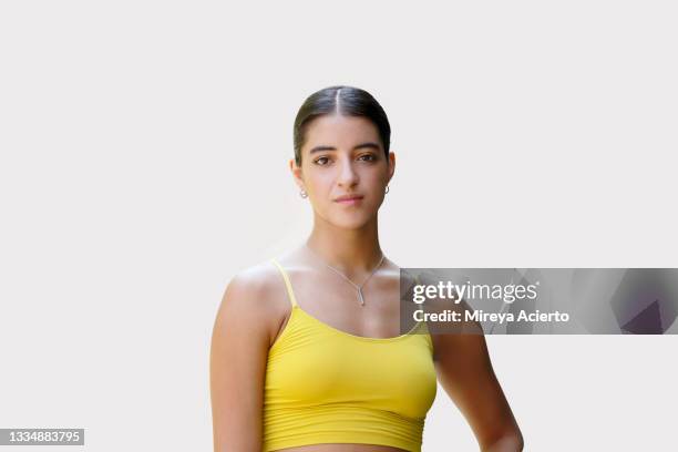 a latinx millennial woman with long hair stands confidently in front of a plain background wearing a yellow sports top and purple leggings. - locket stock pictures, royalty-free photos & images