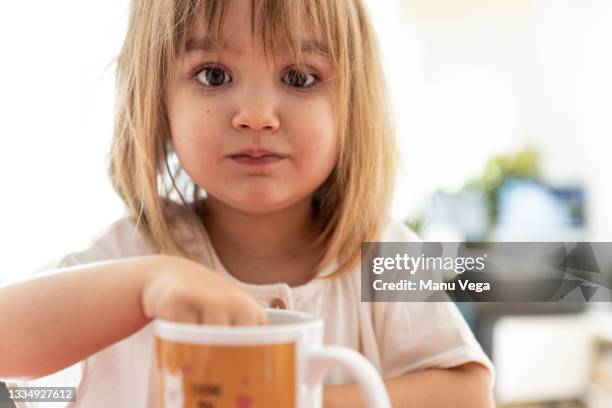 front view of a little girl having breakfast in the kitchen dipping her cookie in the cup. - blonde fille photos et images de collection