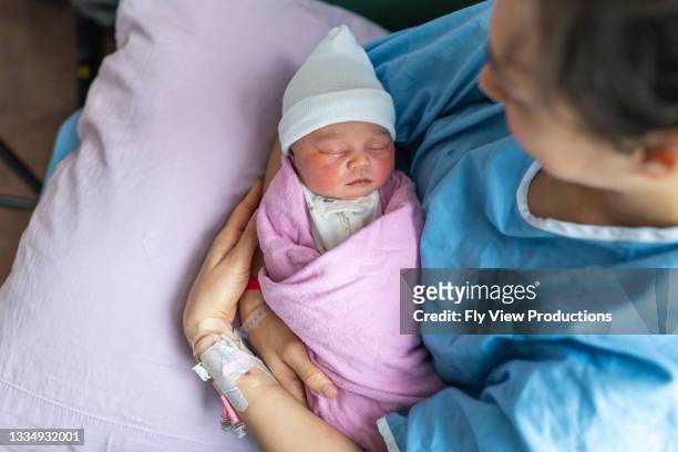 entzückendes neugeborenes baby gemischter rasse, das in den armen der mutter schläft - family photo in the delivery room stock-fotos und bilder