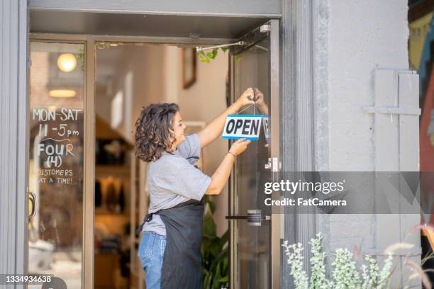 small business owner hanging an open sign at store front - store opening covid stock pictures, royalty-free photos & images