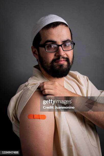 young muslim man posing showing a vaccination band-aid in his arm - name patch stock pictures, royalty-free photos & images