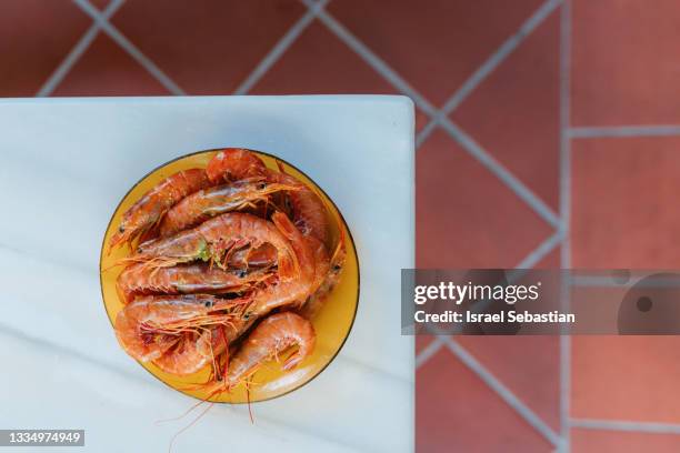 view from above of a plate of shrimps ready to be cooked on the barbecue over an orange glass plate and a marble table. healthy food concept. - bbq shrimp stock pictures, royalty-free photos & images