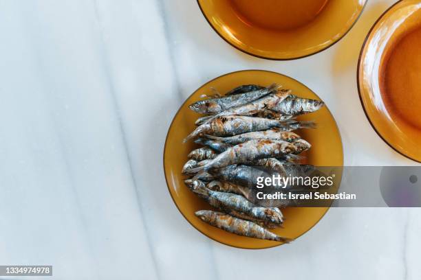 view from above of freshly grilled sardines on orange glass plate and marble table. healthy food concept. - bluefish stock pictures, royalty-free photos & images