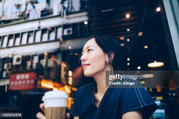 beautiful young asian woman looking through window while enjoying a cup of coffee by window at cafe, with city scene reflected on the window. having a relaxing and carefree moment - enjoying coffee cafe morning light stock-fotos und bilder