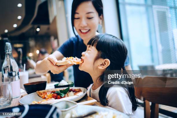 young asian mother and lovely little daughter having lunch, eating freshly served pizza in restaurant. family enjoying a happy meal together. family and eating out lifestyle - children restaurant stockfoto's en -beelden