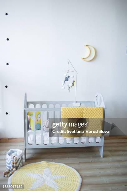 baby room with wooden gray bed, yellow textile plaid on it. mobile with wool colorful dragons, moon lamp on the wall and knitted rug with star ornament on the floor. - babybett stock-fotos und bilder