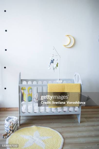 baby room with wooden gray bed, yellow textile plaid on it. mobile with wool colorful dragons, moon lamp on the wall and knitted rug with star ornament on the floor. - using mobile stockfoto's en -beelden