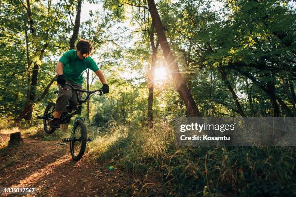 at the forest, skilled teenage boy, jumping from small uphill with his bmx bike - bmx park stock pictures, royalty-free photos & images
