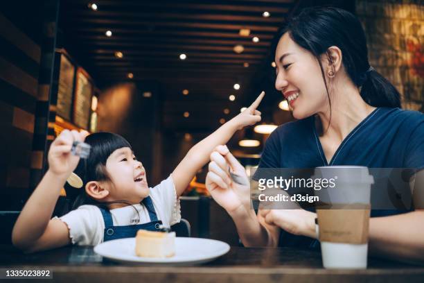 young asian mother and lovely little daughter sharing a slice of cheese cake in cafe, chatting and having an intimate bonding time together and smiling joyfully - asian family cafe stockfoto's en -beelden