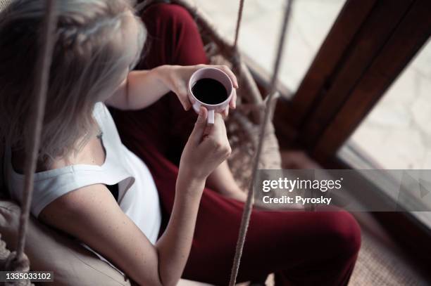 a woman relaxing in a comfortable rope swing in the living room - modern cottage stock pictures, royalty-free photos & images
