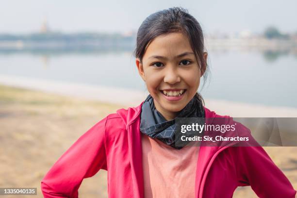 portrait of young smilling asian girl wearing pink jacket standing in the park at outdoors - filipino girl stockfoto's en -beelden