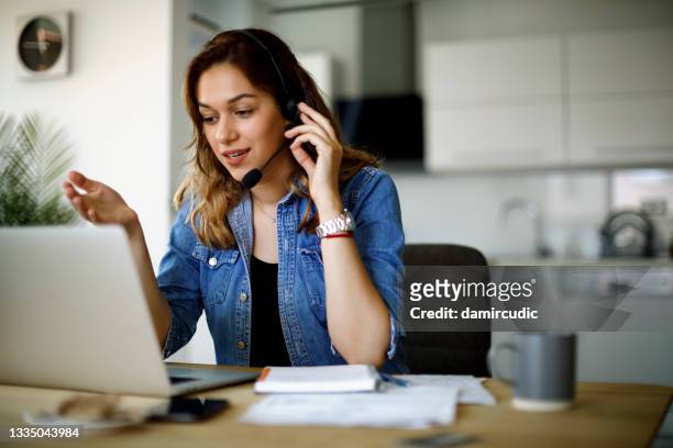giovane donna che usa un auricolare e un laptop in ufficio - hands free device foto e immagini stock