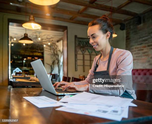 business owner working at a restaurant doing the bookkeeping using her laptop - food company manager stock pictures, royalty-free photos & images