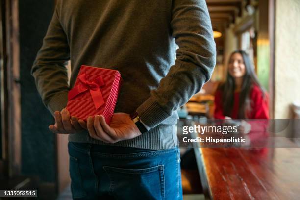 man surprising woman with a gift while celebrating valentines at a restaurant - valentijnsdag stockfoto's en -beelden