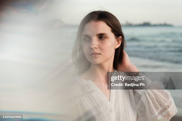 portrait of young cute woman in white blouse with dark hair, blue eyes and freckles - blusa beige fotografías e imágenes de stock