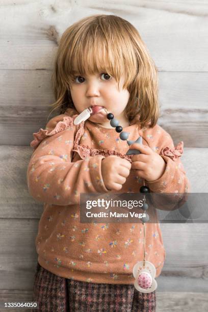 cute baby girl looking at the camera while biting the pacifier string - baby accessories the dummy stock pictures, royalty-free photos & images