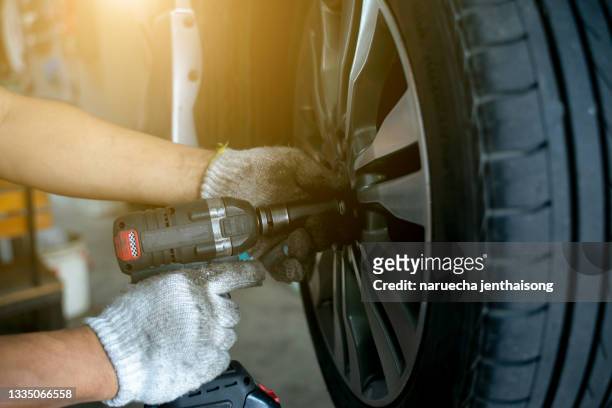 detail image of mechanic hands with tool, changing tyre of car, with blurred background of garage. - neumaticos fotografías e imágenes de stock