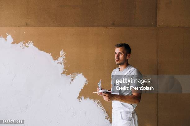 portrait of a serious young man plastering wall in his workshop - plasterer stock pictures, royalty-free photos & images