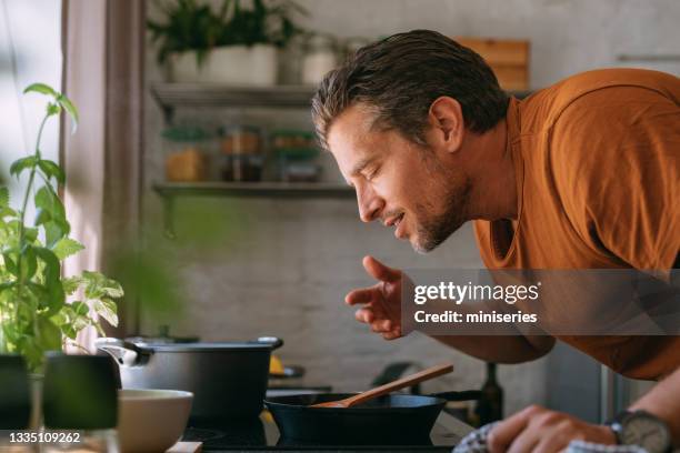 handsome young man enjoying the aroma of a meal in a kitchen - smelling 個照片及圖片檔