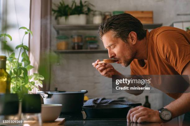 handsome young man tasting the meal in a kitchen - smelling food stock pictures, royalty-free photos & images