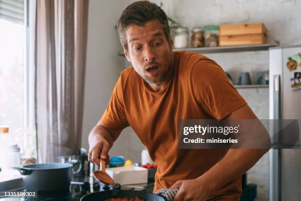handsome man looking surprise while holding a hot pan and a wooden spoon - ignorance stockfoto's en -beelden