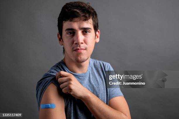 young man posing showing his vaccination band-aid in his arm - young adult vaccine stock pictures, royalty-free photos & images