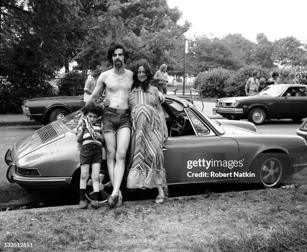 View of a mother and father, with their young son, leaning on their Porsche convertible, in an unidentified public park in Chicago, 1980. The father...