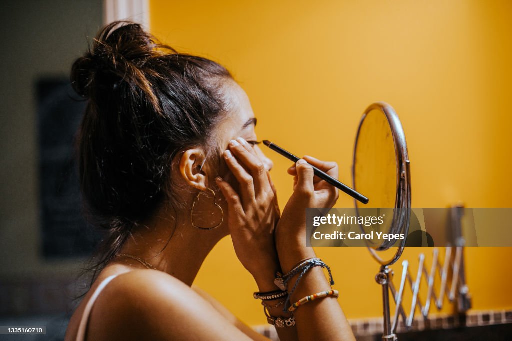 Young teenager applying eyeliner in domestic bathroom