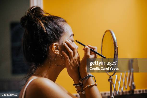 young teenager applying eyeliner in domestic bathroom - lápiz de ojos fotografías e imágenes de stock