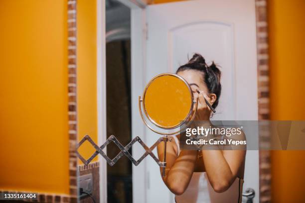 a woman standing close to an illuminated mirror at the bathroom she si applying eyeliner - 鏡台 ストックフォトと画像