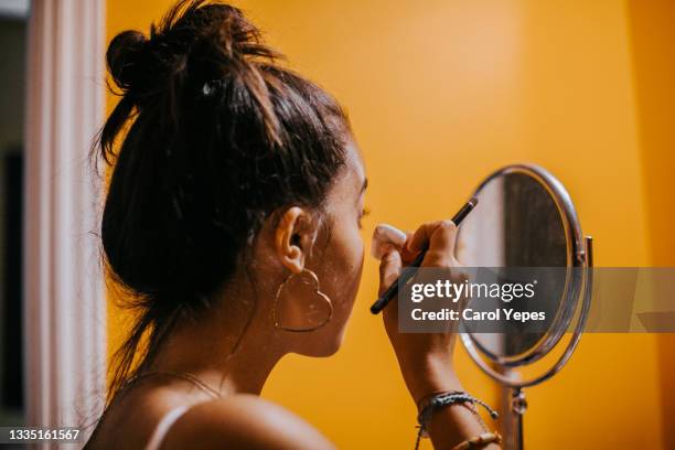 a young woman applies powder foundation in the bathroom in front of the mirror - applying makeup with brush fotografías e imágenes de stock