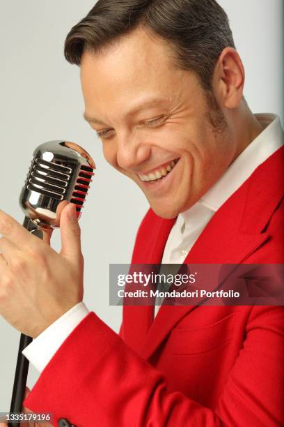 Italian singer Tiziano Ferro with a boom microphone and a red jacket, in the style of the Fifties, smiles to the camera. Italy, December 6th, 2017