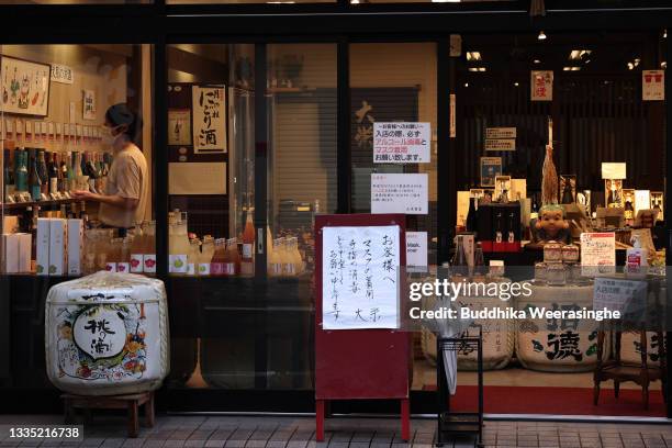 Man wearing a protective face mask arranges bottles of Japanese sake, rice wine inside the alcohol store, bars and restaurants stop serving alcohol...