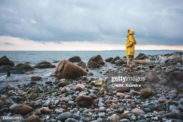 mujer con impermeable amarillo caminando por la playa en un día lluvioso - escena de tranquilidad fotografías e imágenes de stock