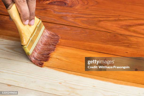 hand holding a brush applying varnish paint on a wooden surface - teak wood material photos et images de collection